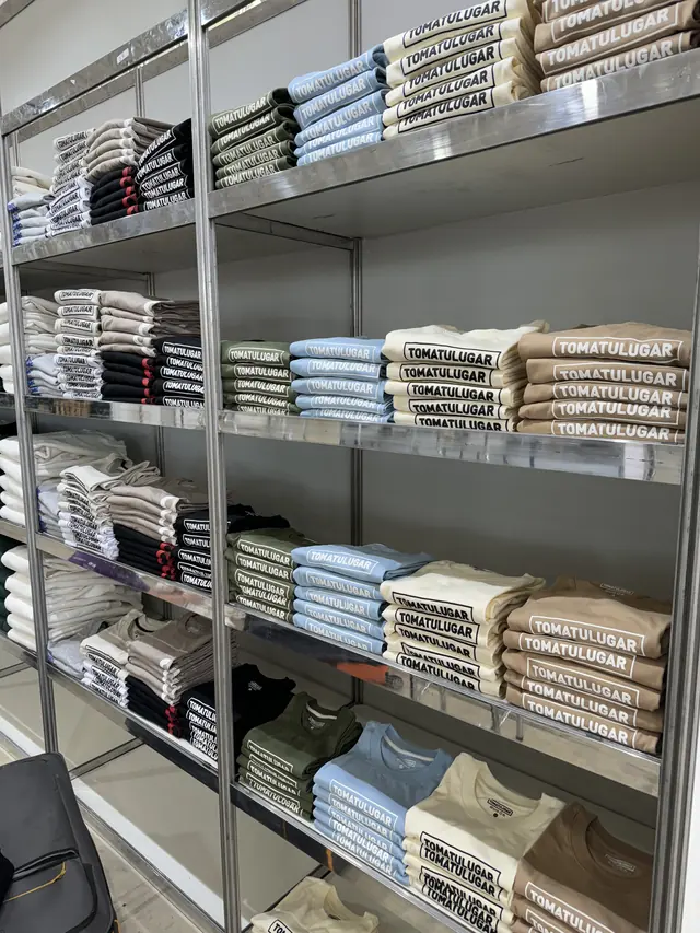 Estantería con remeras estampadas dobladas y separadas por talle para un pedido de merch por mayor