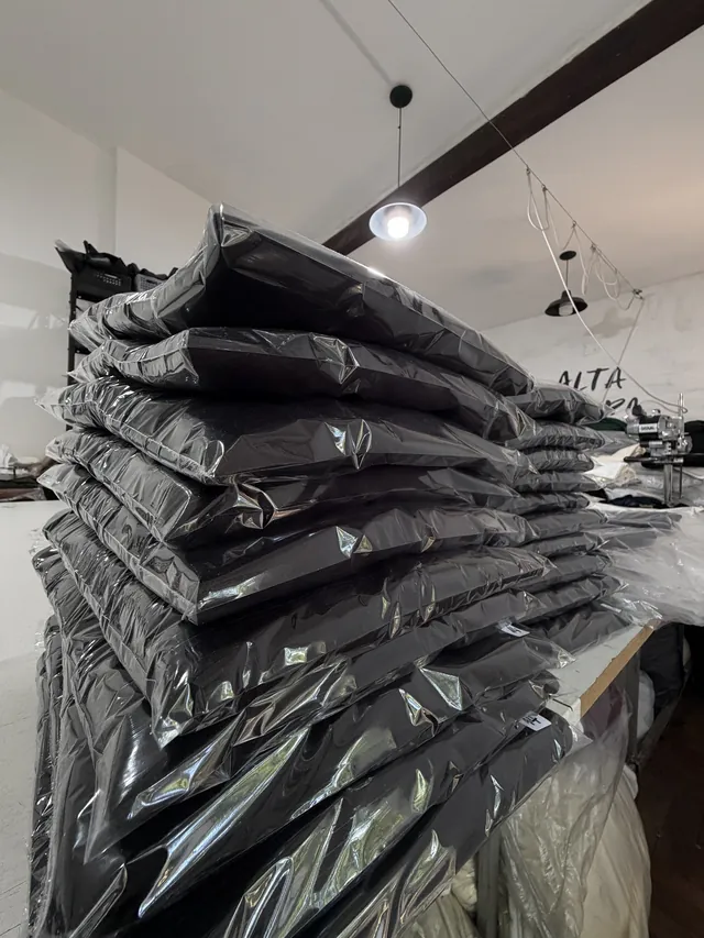 Pila de prendas negras embolsadas en el taller, merch listo para entregar
